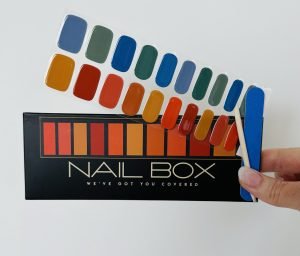 A female hand holding richly coulered blues and red semi cured gel nail sticker kit with nail file sold by Nail Box