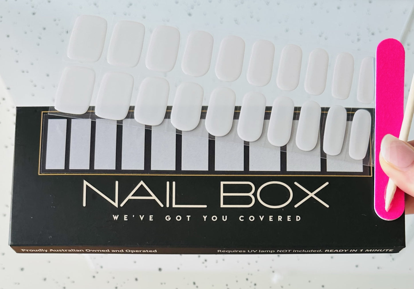 female hand holding silver grey semi cured gel nail kit sold by nail box with file and orange stick